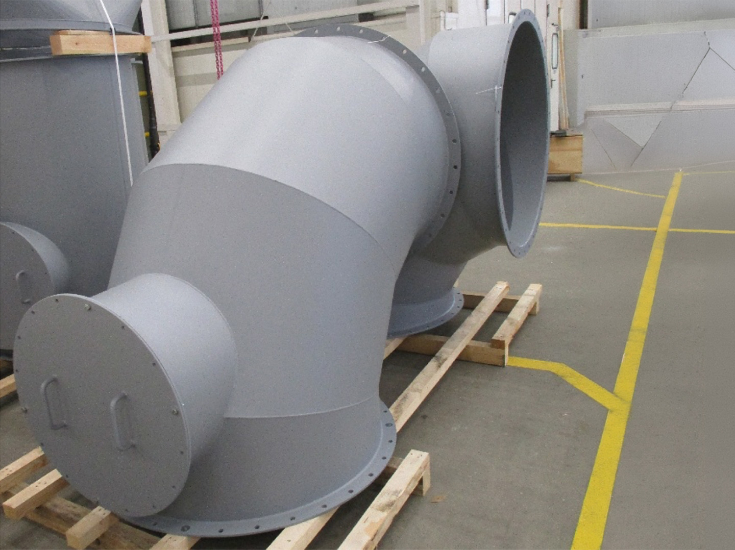 Großes, graues Mischkanal-Bauteil aus Metall auf Holzrahmen in einer Werkhalle.