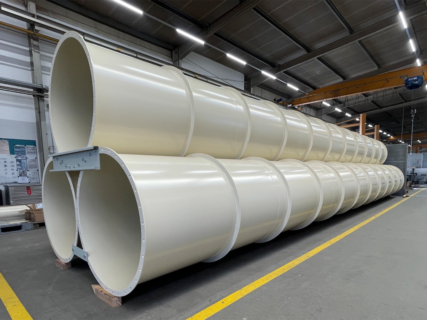 Mehrere große, beigefarbene Rohrsegmente übereinandergestapelt in einer Produktionshalle.