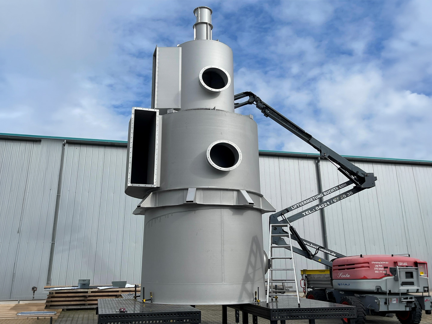 Großer vertikaler Metallbehälter mit mehreren Anschlussöffnungen, montiert im Außenbereich einer Produktionsanlage.